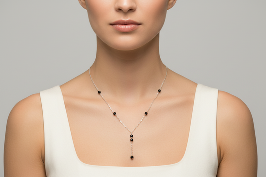 Woman wearing a sterling silver delicate Y necklace with small black beads on a plain background