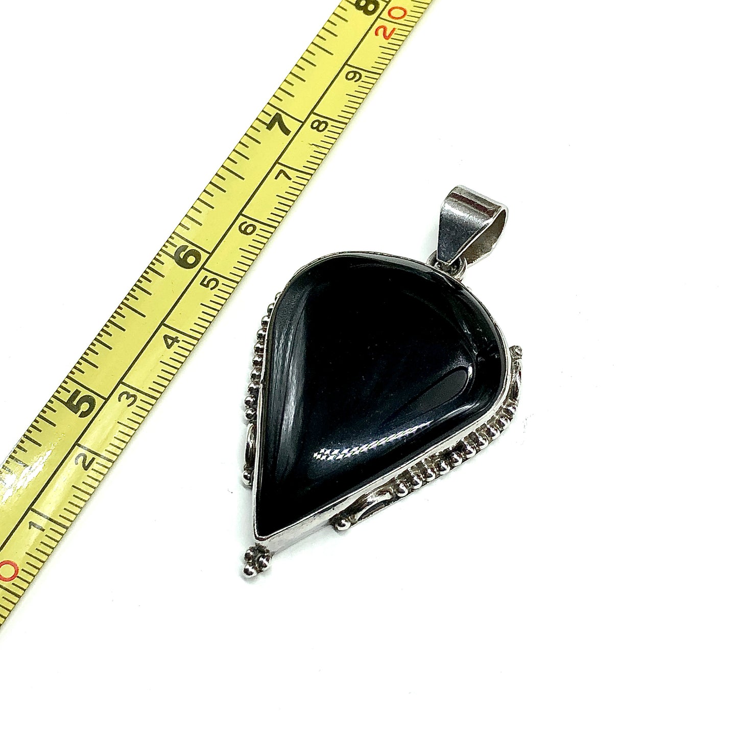 A teardrop-shaped black onyx pendant with a 925 Sterling Silver bezel setting, shown next to a measuring tape
