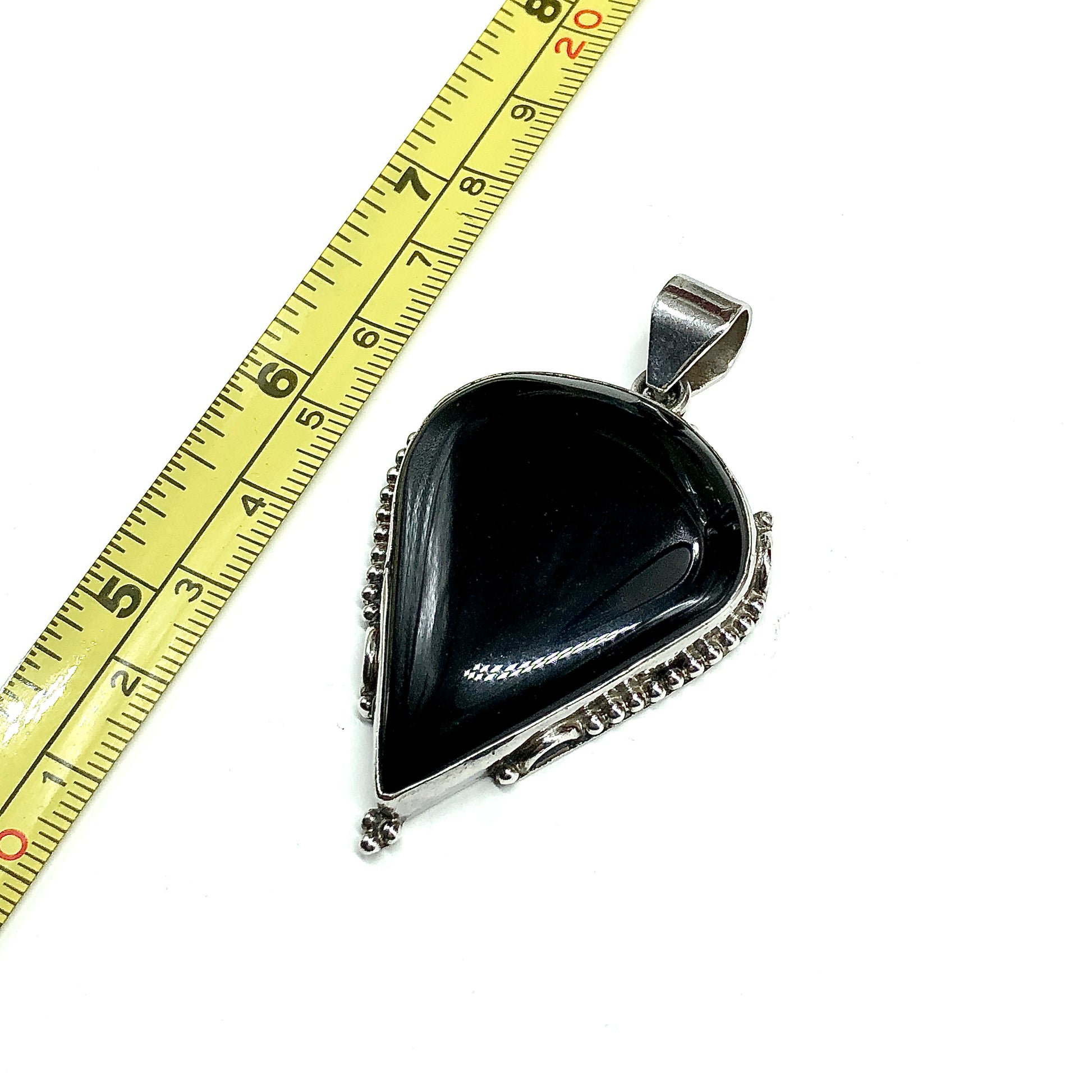 A teardrop-shaped black onyx pendant with a 925 Sterling Silver bezel setting, shown next to a measuring tape