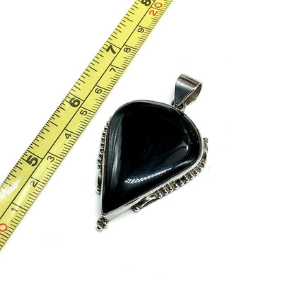 A teardrop-shaped black onyx pendant with a 925 Sterling Silver bezel setting, shown next to a measuring tape