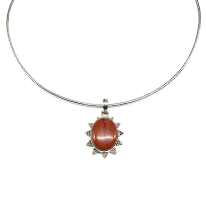 A 925 sterling silver bangle collar necklace featuring an oval brick reddish-brown jasper cabochon stone surrounded by a starburst-like sterling silver setting. Great accessory for men or women.
