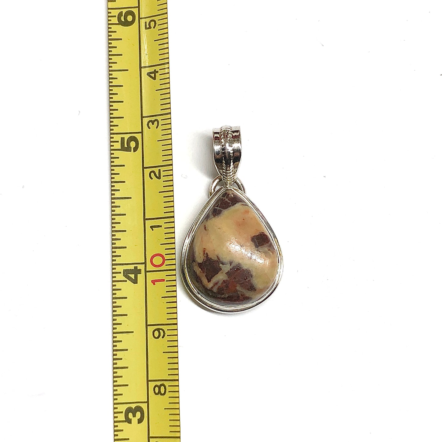 A teardrop-shaped pendant with a 925 sterling silver bezel and bail, featuring a unique marbled stone with cream, brown, and reddish inclusions. The pendant is shown next to a yellow measuring tape ruler on a plain white background.