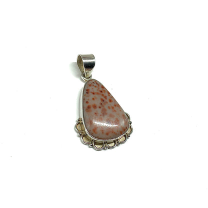 A teardrop-shaped pendant featuring a polished stone with burnt orange speckles on a pale pinkish-beige background, set in a 925 sterling silver bezel setting with decorative scalloped edges and a large bail at the top.