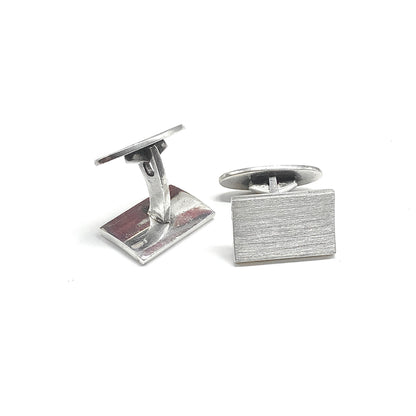 A pair of silver rectangular cufflinks with a brushed metal finish, one showing the front face and the other showing the back mechanism.

